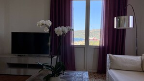 Ett vardagsrum med en tv, ett soffbord med en växt, en soffa och en utsikt genom ett fönster med gardiner.