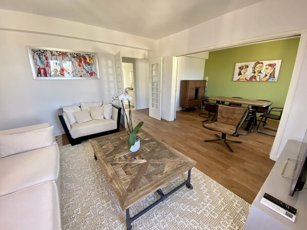 A modern living room with a wooden coffee table, a beige sofa, and a dining area with a wooden table and chairs.