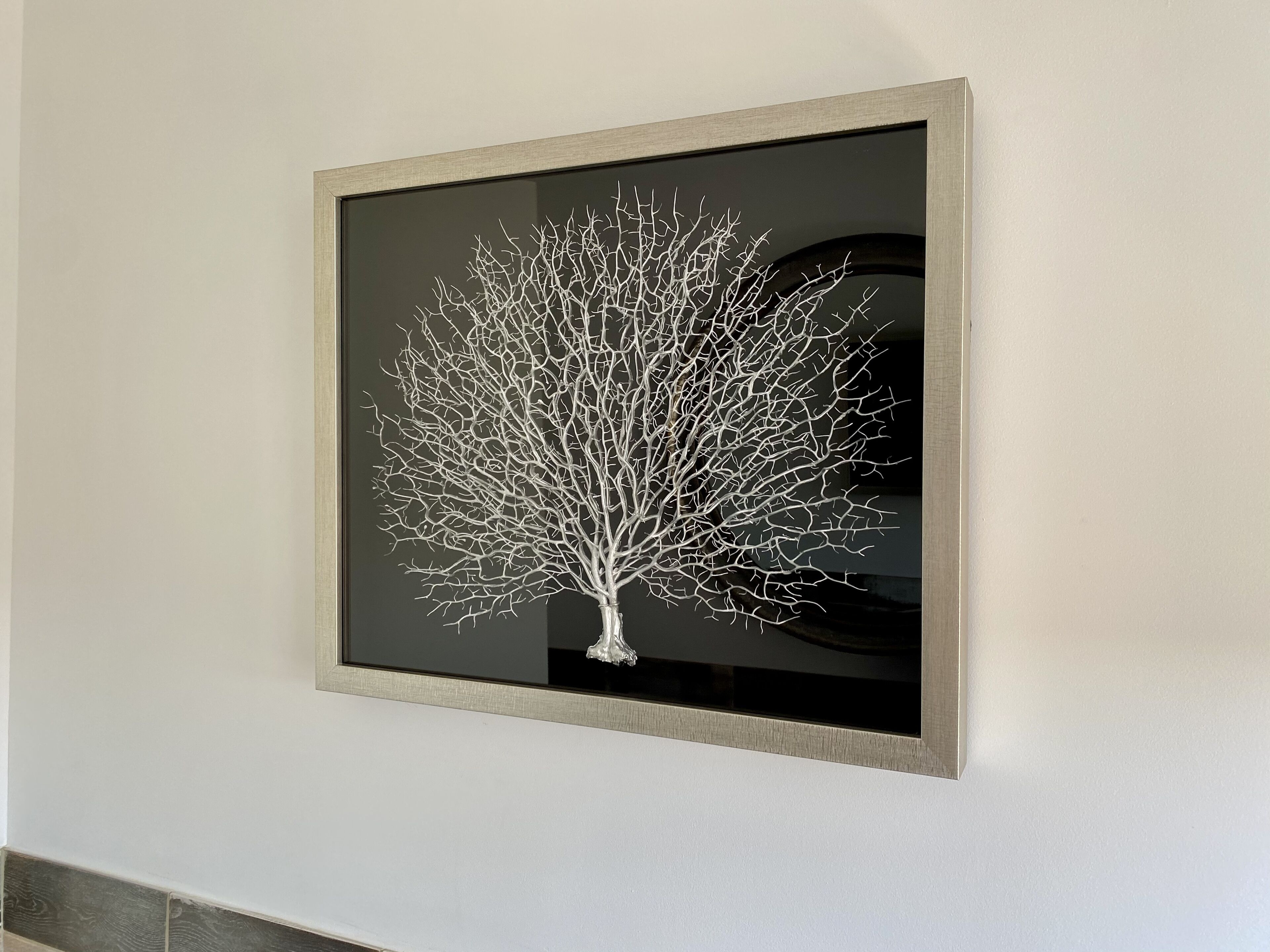 Una obra de arte enmarcada que muestra un árbol en una pared.