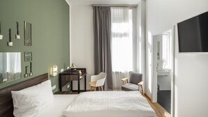 A modern hotel room with a large bed, a desk, a chair, a TV, and a window with curtains. - acor Boutique Hotel (Heidelberg)