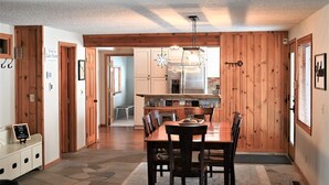 A wooden-paneled dining area with a central table and chairs, a hanging light fixture, and a view into the kitchen. - Lake Front, Lake Charlevoix, Large Park like setting. (Boyne city)