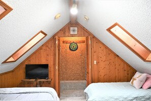 A bedroom with a sloped ceiling, wooden paneling, a television, a bed, and a dartboard. - Lake Front, Lake Charlevoix, Large Park like setting. (Boyne city)