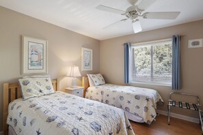 A bedroom with two beds, a ceiling fan, a window with curtains, and artwork on the walls.