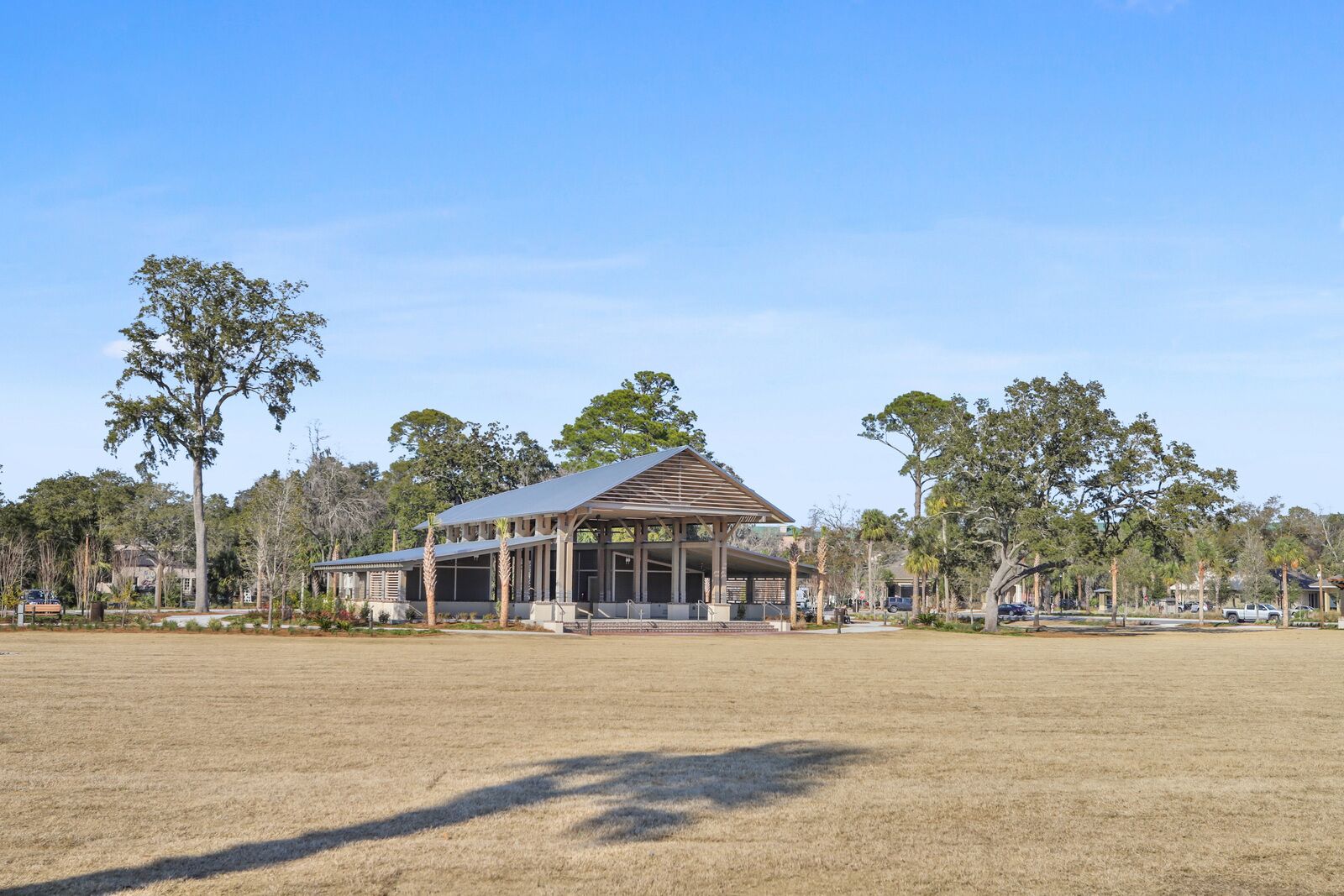 A large, open building with a covered patio area, surrounded by trees and a grassy field.