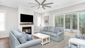 Ein modernes Wohnzimmer mit Kamin, Deckenventilator und großen Fenstern mit Blick ins Freie.