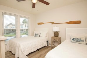 Een slaapkamer met twee bedden, een plafondventilator, een nachtkastje met een lamp en een wandgemonteerde peddel.