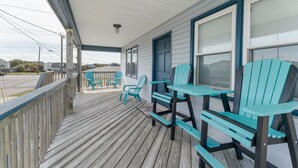Une terrasse en bois avec des fauteuils Adirondack de couleur turquoise et une table, une véranda et une maison avec une porte et des fenêtres bleues.