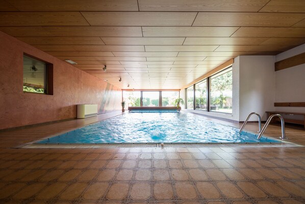 En indendørs swimmingpool med flisegulv, træloft og store vinduer.