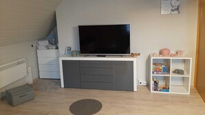 Quarto com televisão em unidade de entretenimento branca, pequena prateleira com brinquedos e radiador na parede.