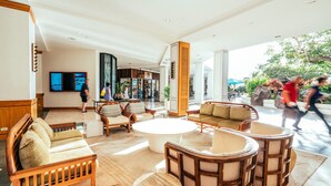 A spacious lobby with a central coffee table surrounded by wooden sofas and armchairs, a large TV screen, and a view of the outdoor area. - Ocean-Marina Views PH at Ilikai Hotel by the Beach w/Full Kitchen & Free WiFi (Honolulu)