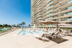 Un espace piscine d’hôtel doté de plusieurs niveaux de balcons, de chaises longues et de parasols.