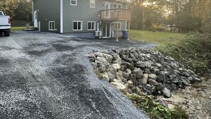 Un bâtiment à deux étages avec une allée gravillonnée et un mur en pierre.