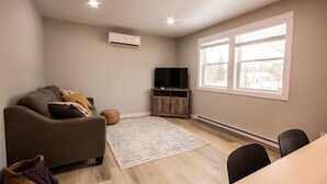 Un salon moderne avec un canapé, un téléviseur à écran plat, un meuble en bois et une grande fenêtre.