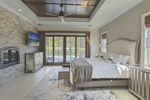 A bedroom with a large bed, a ceiling fan, a fireplace, and a view of a pool through the glass doors.