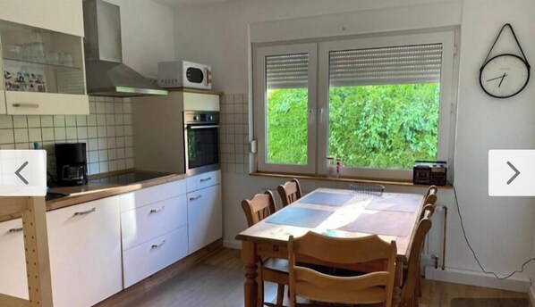 Enjoy meals in this kitchen with a dining table for four, appliances, and a large window overlooking lush greenery.