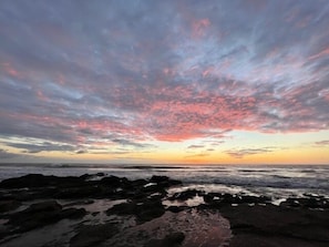 Une plage avec un rivage rocheux et un ciel au coucher du soleil aux couleurs vives.