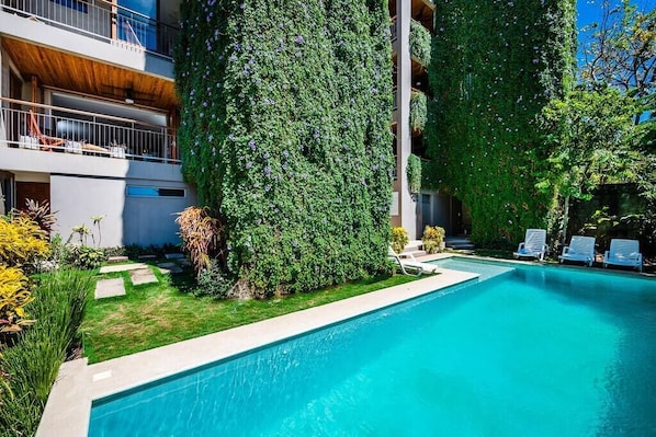 Un bâtiment moderne doté d’une piscine, entouré d’une végétation luxuriante et d’une pelouse bien entretenue.