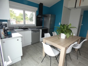 Una cocina moderna con armarios blancos, una campana extractora negra, un refrigerador de acero inoxidable y una mesa de comedor de madera con sillas blancas.