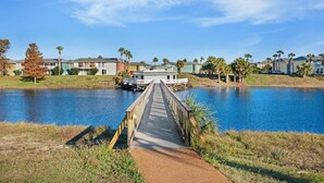 A wooden bridge over a calm body of water, leading to a row of colorful buildings with a clear sky above. - 5 minute to the public beach (Destin)