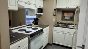 A compact kitchen with white cabinets, a stove, microwave, and a refrigerator. - 5 minute to the public beach (Destin)