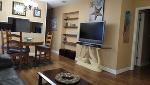 A living room with a TV on a stand, wooden chairs, a dining table, and a sofa. - 5 minute to the public beach (Destin)