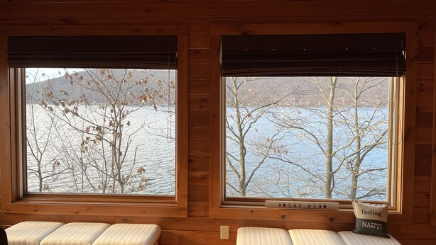 Eine Holzhütte mit zwei Fenstern, die Blick auf einen See und Bäume bietet, mit Holzbanken und einem Thermostat am Fensterbrett.