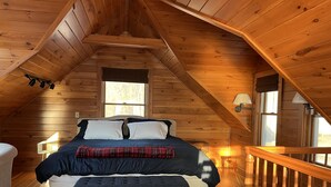 Ein gemütliches Schlafzimmer im Dachgeschoss mit schrägverlegtem Holzboden, einem großen Bett mit Karo-Decke und einem Holzbalkon.