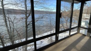 Ein Zimmer mit großen Fenstern und Blick auf einen See und Bäume.