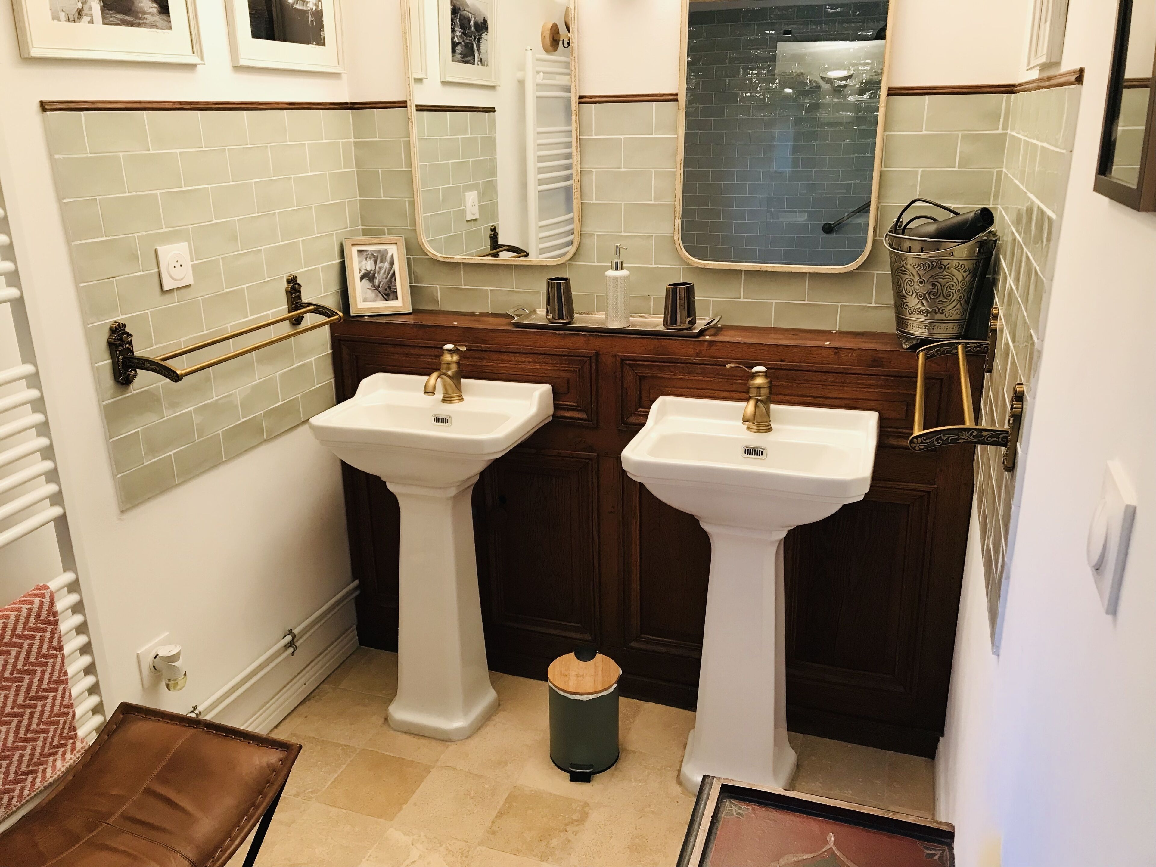Une salle de bain avec deux lavabos sur pied, un porte-serviettes, un miroir et une poubelle.