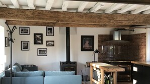 Un salon chaleureux avec un canapé bleu, une table en bois, une cheminée et un coin cuisine doté d’un mur en briques et d’une cheminée.