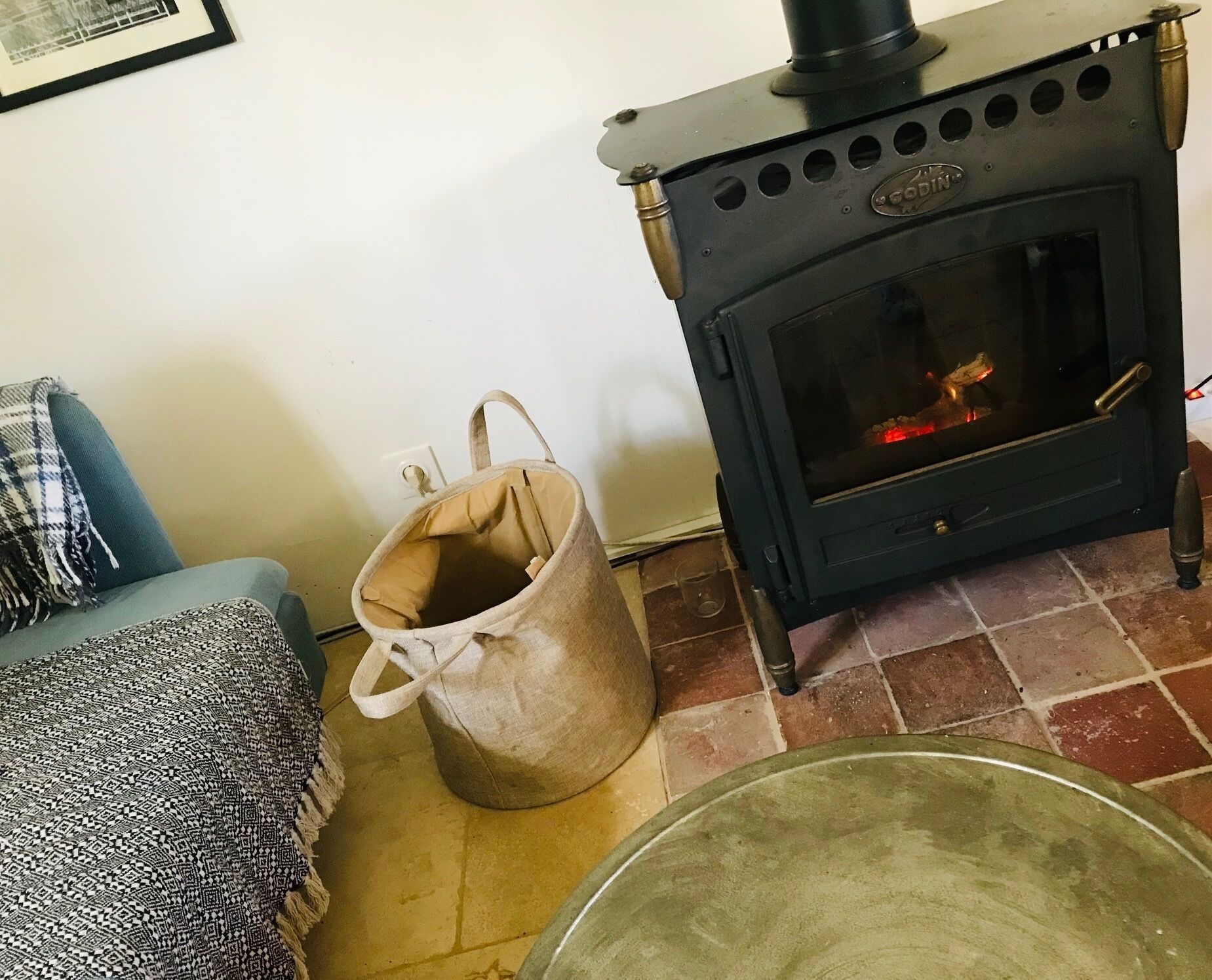 Una habitación con un estufa de leña negra, un sofá azul y una bolsa color beige en el suelo.