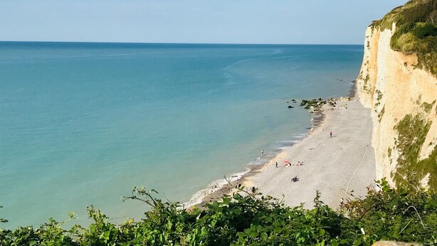Une plage côtière avec une falaise, une eau claire et quelques personnes.