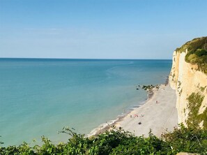 A coastal beach with a cliff, clear water, and a few people.