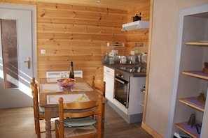 A compact kitchen with wooden walls, a dining table with chairs, and a built-in oven. - Chez Paulette and Henri Guesthouse—Accommodation for 2 people, 2-star rating, Alsace Tourism Label (STEIGE)