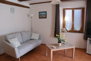 A living room with a grey sofa, a wooden coffee table with a potted plant, a floor lamp, and a window with curtains. - Chez Paulette and Henri Guesthouse—Accommodation for 2 people, 2-star rating, Alsace Tourism Label (STEIGE)
