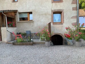 A building with a rustic exterior, a wooden door, and a small garden area with potted plants and flowers. - Chez Paulette and Henri Guesthouse—Accommodation for 2 people, 2-star rating, Alsace Tourism Label (STEIGE)