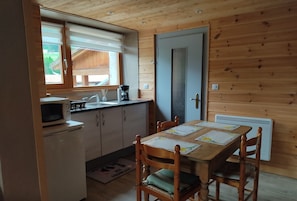 A compact kitchen with a microwave, sink, and wooden cabinets. A dining table with chairs is positioned in front of a door. - Chez Paulette and Henri Guesthouse—Accommodation for 2 people, 2-star rating, Alsace Tourism Label (STEIGE)