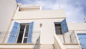 A building with a white facade, blue shutters, and a small balcony with a metal railing. - Casa Greta (San Vito Lo Capo)