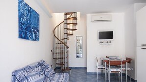 A modern living room with a spiral staircase, a dining area with a TV, and a large abstract painting on the wall. - Casa Greta (San Vito Lo Capo)