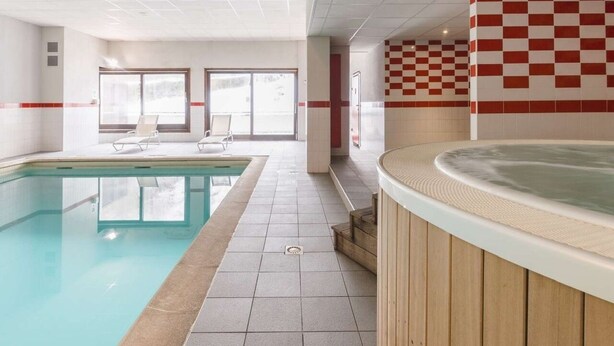 Une piscine intérieure dotée d’un jacuzzi, de murs carrelés et d’un mur orné d’un motif à carreaux.