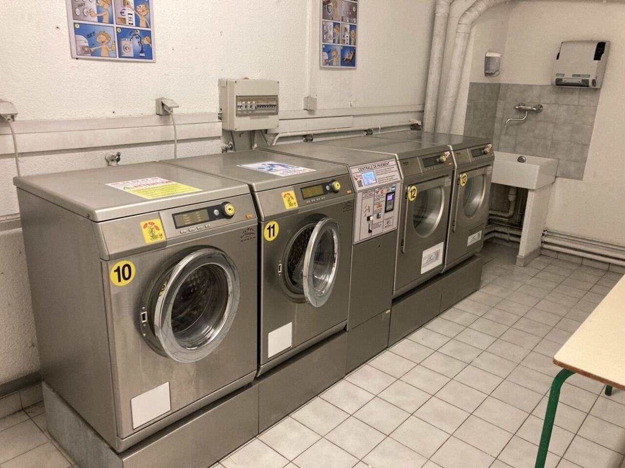 A row of four front-loading washing machines in a public laundry facility, each with a numbered control panel.
