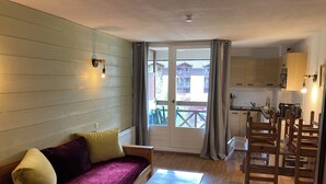 Un salon chaleureux avec un canapé en bois, une petite table en bois et une cuisine en arrière-plan.