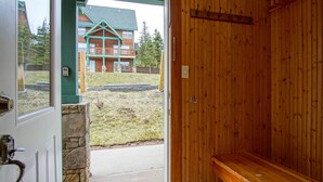 A wooden interior with a bench, a stone wall, and a view of a green-roofed building outside. - Camp Four 23: Pet Friendly,  Slope side, Gas Fireplace. (Snowshoe)