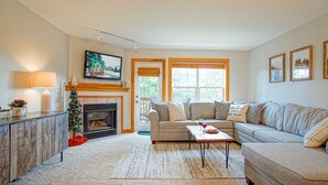 A cozy living room with a fireplace, a sofa, a coffee table, and a TV mounted on the wall. - Camp Four 23: Pet Friendly,  Slope side, Gas Fireplace. (Snowshoe)