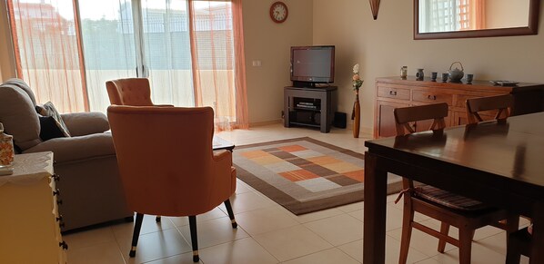 A living room with a sofa, armchair, TV, wooden cabinet, and dining table.