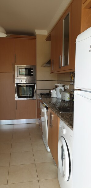 A kitchen with wooden cabinets, a built-in oven, a microwave, a washing machine, and a sink.