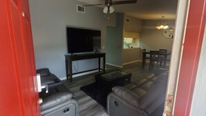 Una sala de estar con televisor de pantalla plana, sofás de cuero, una mesa de centro de vidrio y un comedor con mesa y sillas.