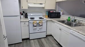 Una cocina moderna con armarios blancos, un lavamanos de acero inoxidable, un microondas, una estufa y un lavavajillas.