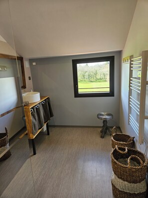 A bathroom with a large window, a wooden bench with towels, a small stool, and wicker baskets. - Renovated stone barn with swimming pool between Lot and Dordogne (PAYRIGNAC)