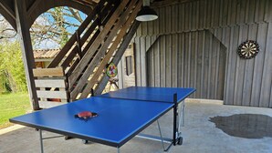 Un tavolo da ping pong con racchetta, allestito all'aperto con una struttura in legno e un bersaglio da freccette sullo sfondo.